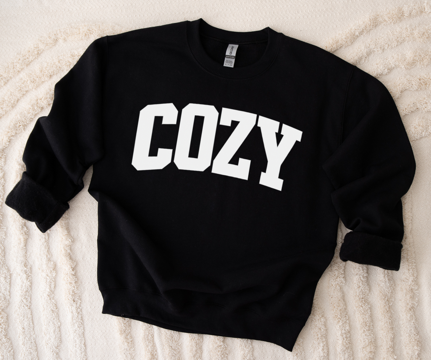 Black sweatshirt with 'COZY' text on a textured beige surface