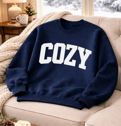 Navy blue sweatshirt with 'COZY' text on a beige couch in a cozy living room.