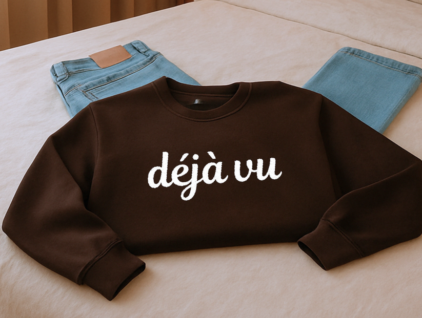 Brown sweatshirt with 'déjà vu' text on a beige surface with jeans in the background