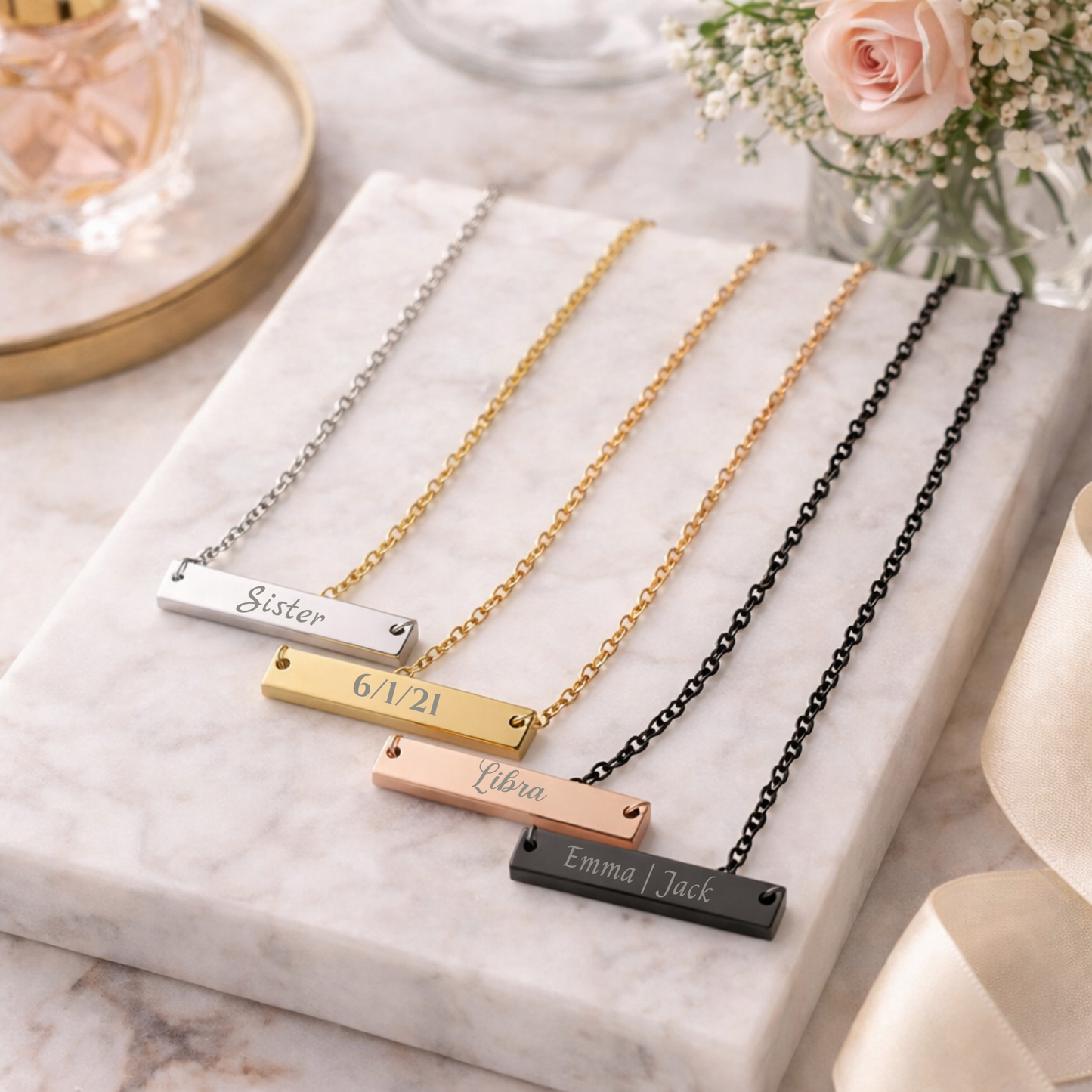 Four necklaces with engraved names on a marble surface.