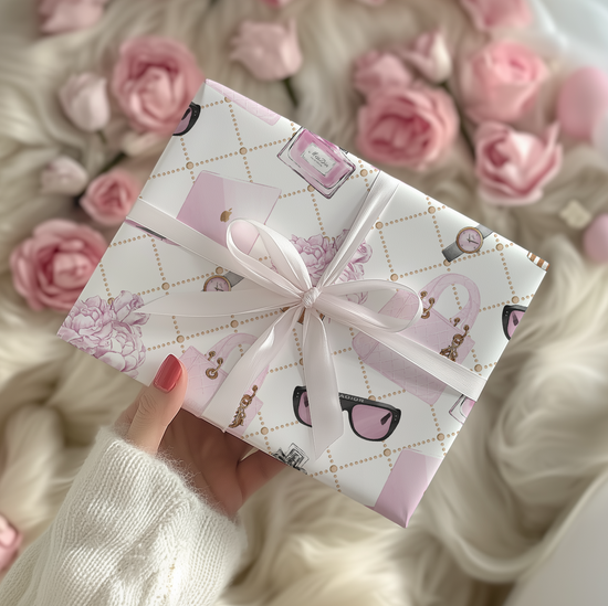 Gift box with wrapping paper showing fashion accessories with pink ribbon held by a person against a background of pink roses.