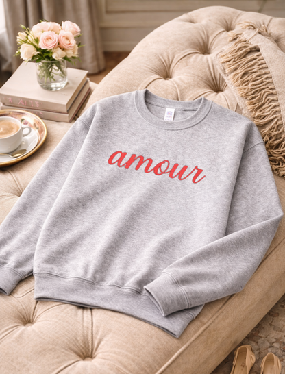 Gray sweatshirt with 'amour' text on a beige couch with a cup of coffee and flowers in the background.