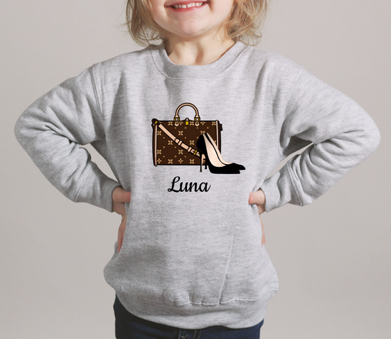 Child wearing a gray sweatshirt with a design and the name 'Luna' on a plain background