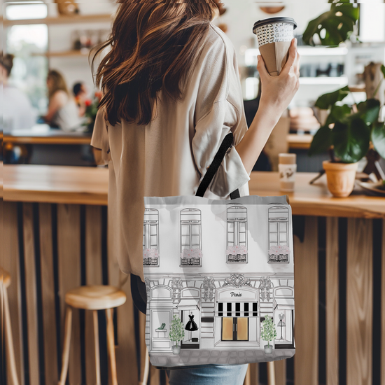 Person holding a tote bag with building design in a cafe