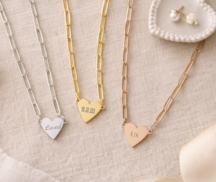 Three heart-shaped necklaces with engraved text on a textured surface.