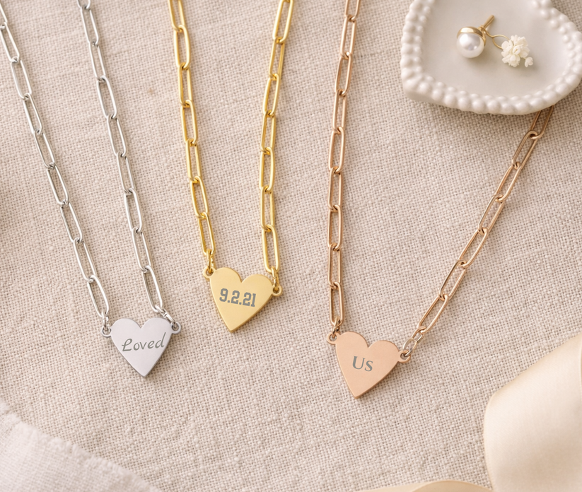 Three heart-shaped necklaces with engraved text on a textured surface.