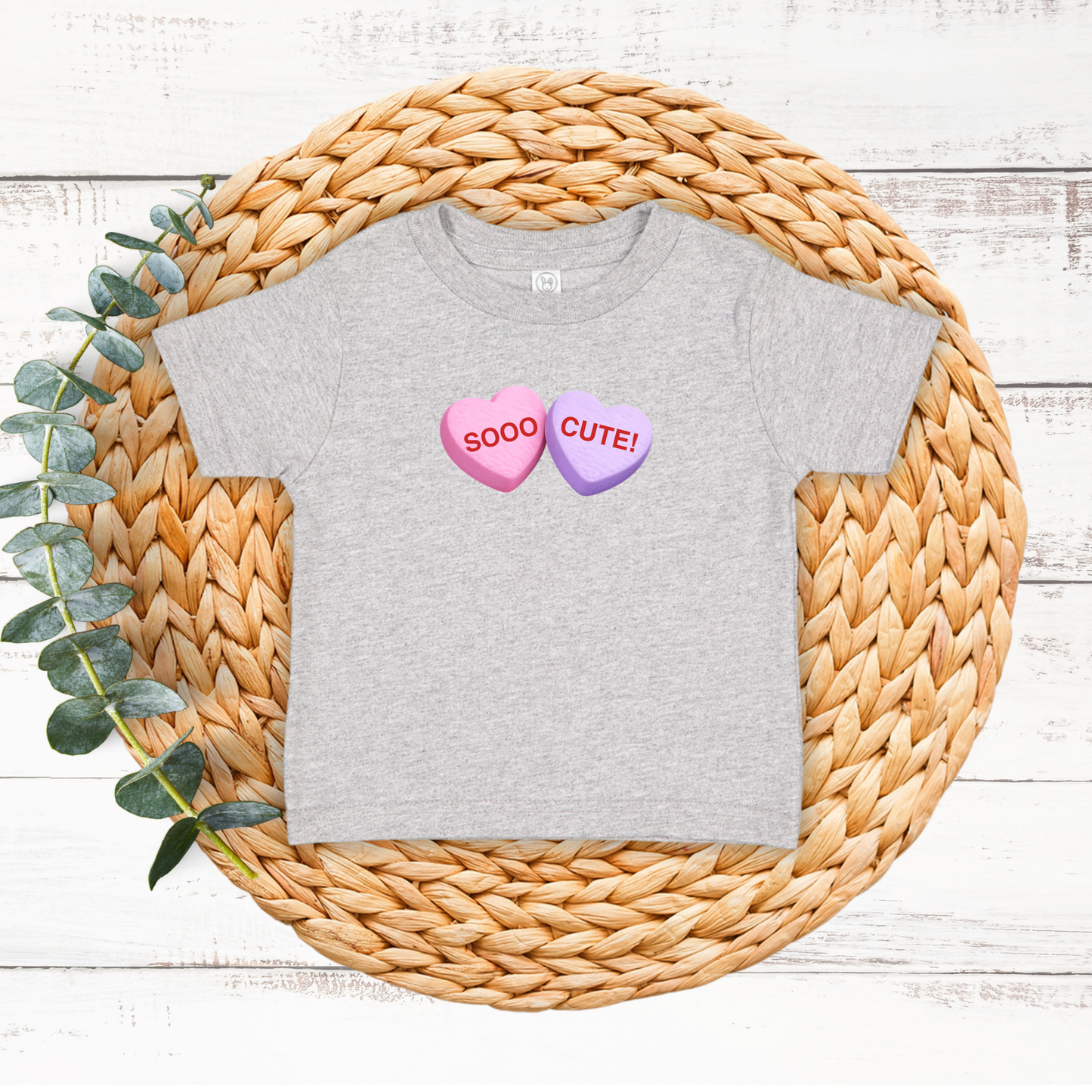 Gray t-shirt with heart-shaped candy designs and text on a woven mat