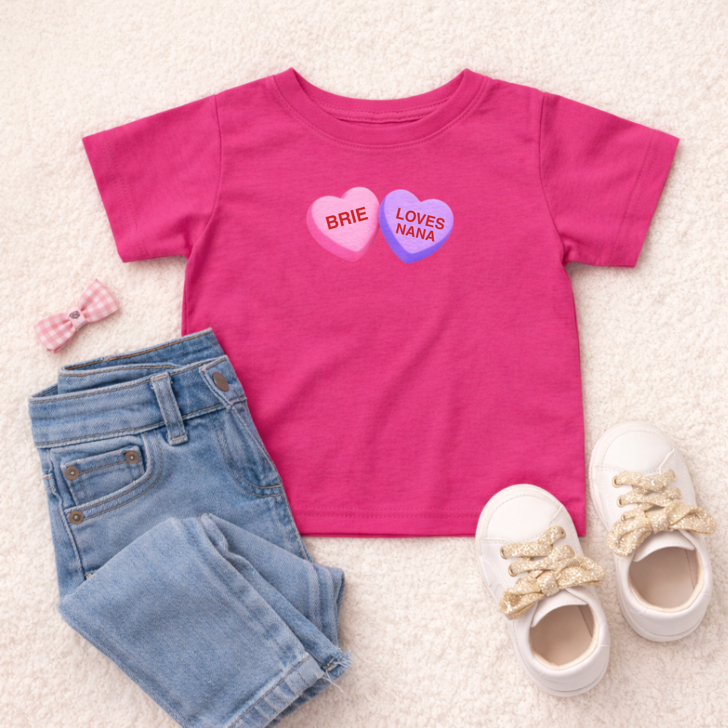 Pink t-shirt with heart designs, blue jeans, and white shoes on a light background