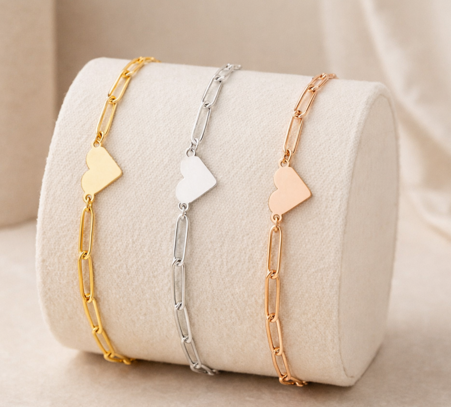 Three heart-shaped bracelet options on a cylindrical white stand against a beige background
