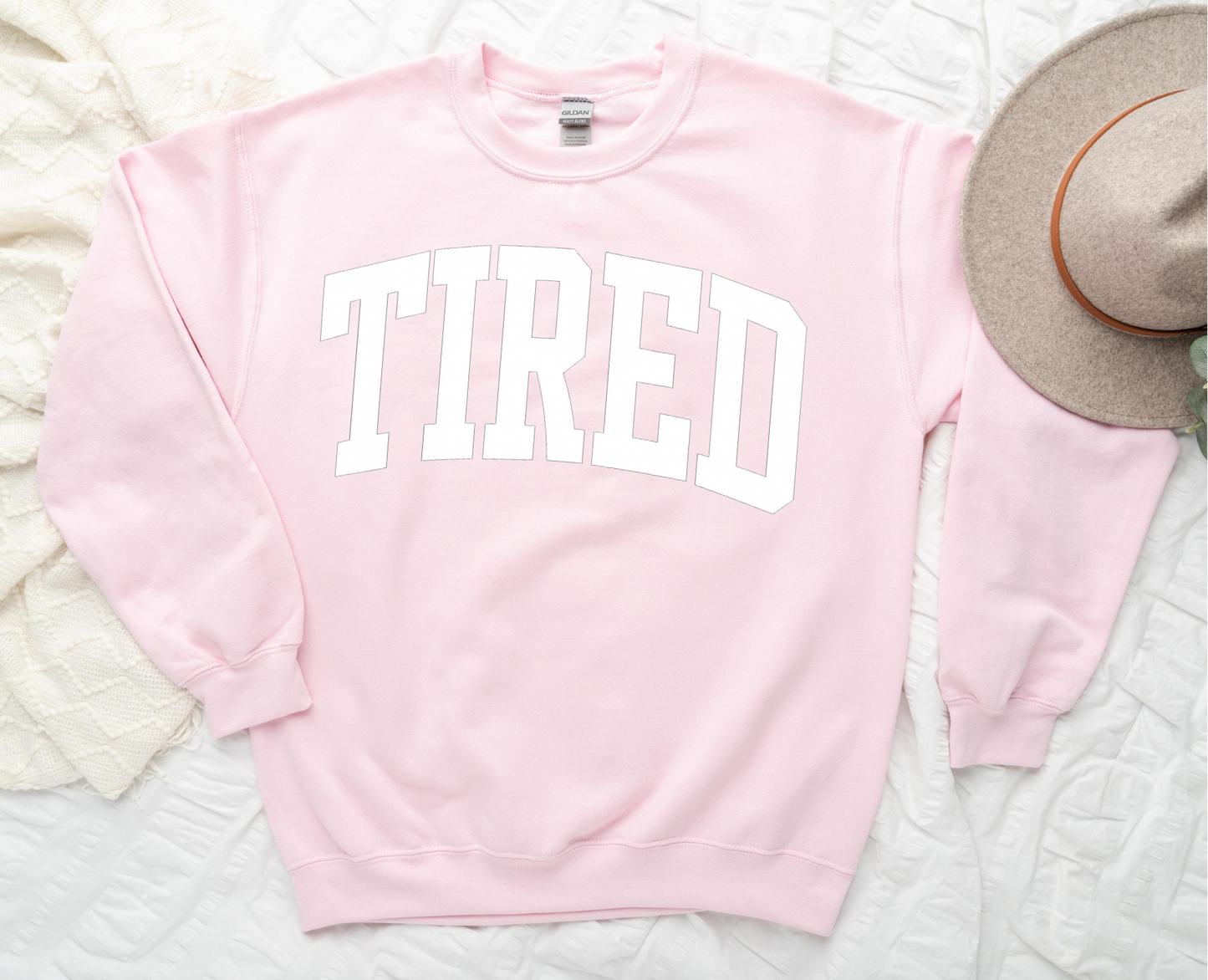 Pink sweatshirt with 'TIRED' text on a textured surface