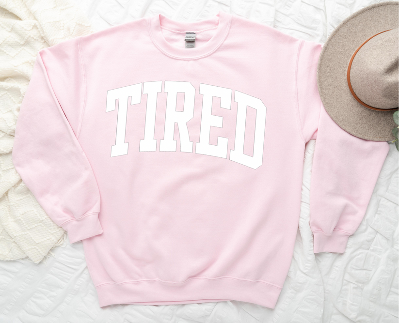 Pink sweatshirt with 'TIRED' text on a textured surface