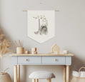 Nordic-style nursery with a monogrammed wall banner featuring a bear in an orchard, desk, stool, and decorative items.