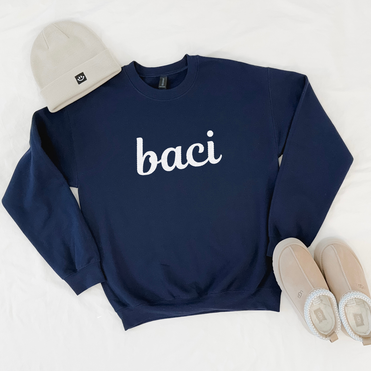 Navy blue sweatshirt with 'baci' text, beige beanie, and shoes on a white background