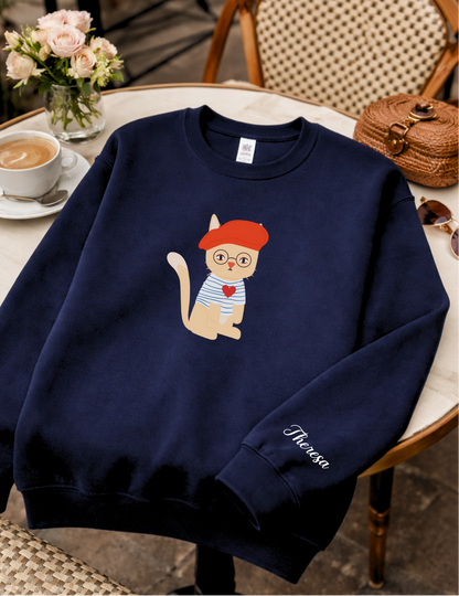 Navy blue sweatshirt with a cartoon cat design on a chair in a cafe setting
