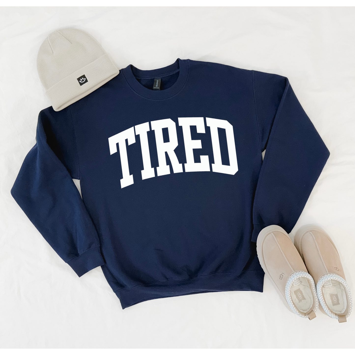 Navy sweatshirt with 'TIRED' text, beige beanie, and beige shoes on a white background