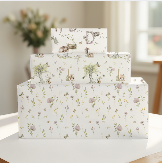 Set of three boxes stacked on a table with a blurred background. Top two boxes have monogrammed woodland animals themed paper.  Bottom box has meadow flower wrap.