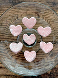 Pink heart-shaped mini marshmallows on a glass plate with a wooden background