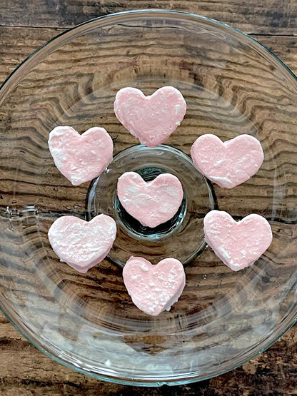 Pink heart-shaped mini marshmallows on a glass plate with a wooden background