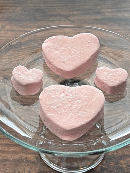 Pink heart-shaped marshmallows on a glass plate with a wooden 