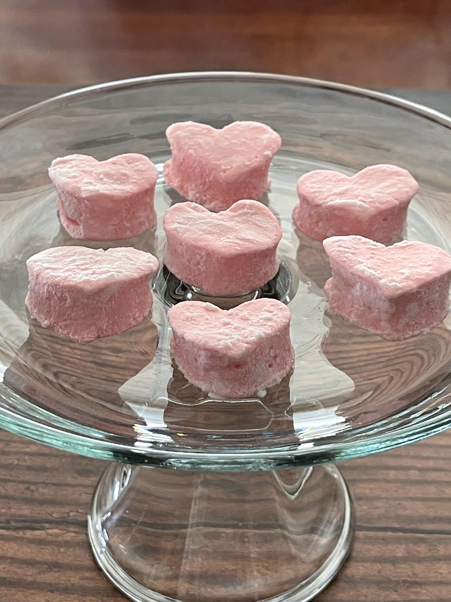 Pink heart-shaped mini marshmallows on a glass plate with a wooden 