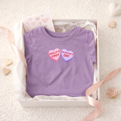 Purple t-shirt with 'Holly's First Valentine's Day' text in a box on a light background