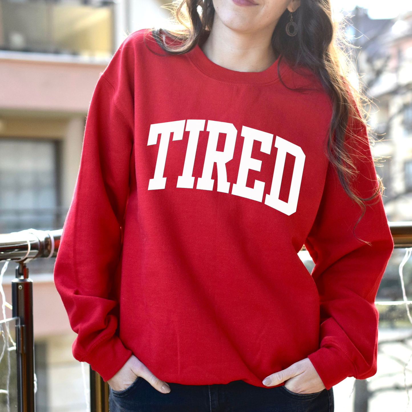 Person wearing a red sweatshirt with 'TIRED' printed on it, standing outdoors.