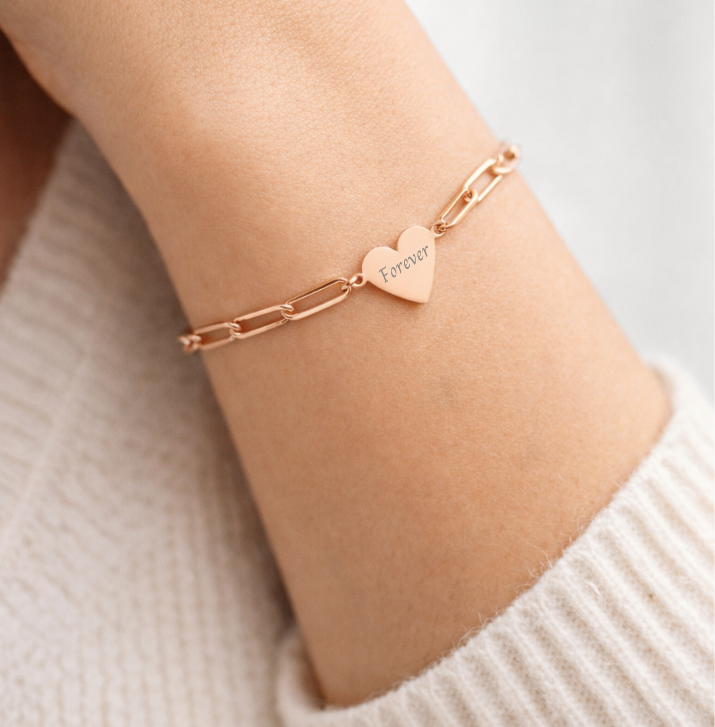 Rose gold bracelet with a heart-shaped tag on a wrist against a neutral background