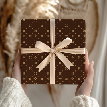 Brown gift box with tan pattern and white ribbon held by hands against a blurred background