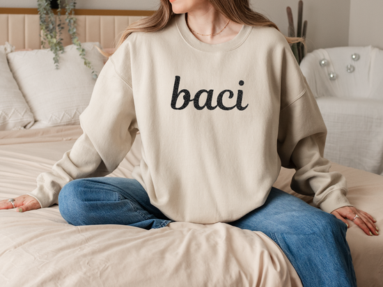 Person wearing a beige sweatshirt with 'baci' text, sitting on a couch.