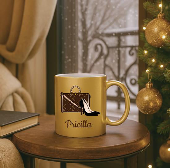 Gold mug with a shoes and purse and name 'Pricilla' on a wooden table with a Christmas tree in the background.