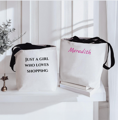 Two white tote bags with text and a name, placed on a white surface.