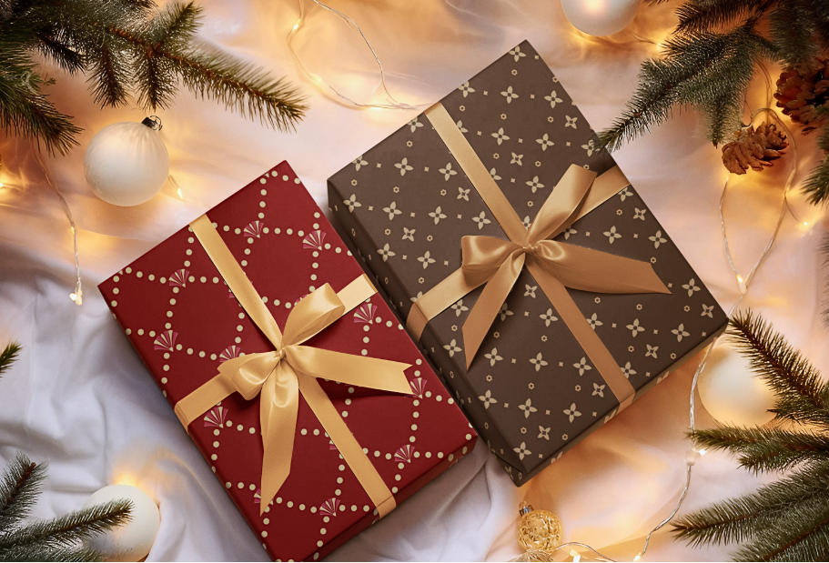 Two gift boxes with gold ribbons on a festive background with Christmas decorations.
