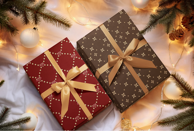 Two gift boxes with gold ribbons on a festive background with Christmas decorations.