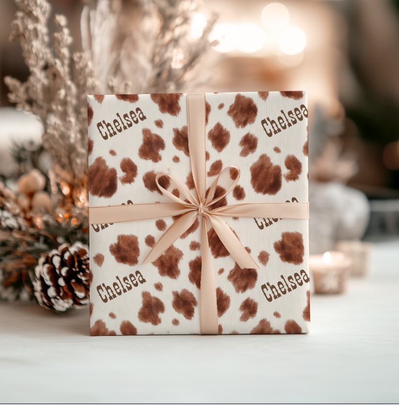 Gift box with brown appaloosa pattern and 'Chelsea' text, tied with a beige ribbon, on a blurred decorative background.