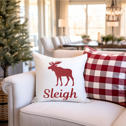 Decorative pillow with a moose design and 'Sleigh' text on a couch in a living room setting.