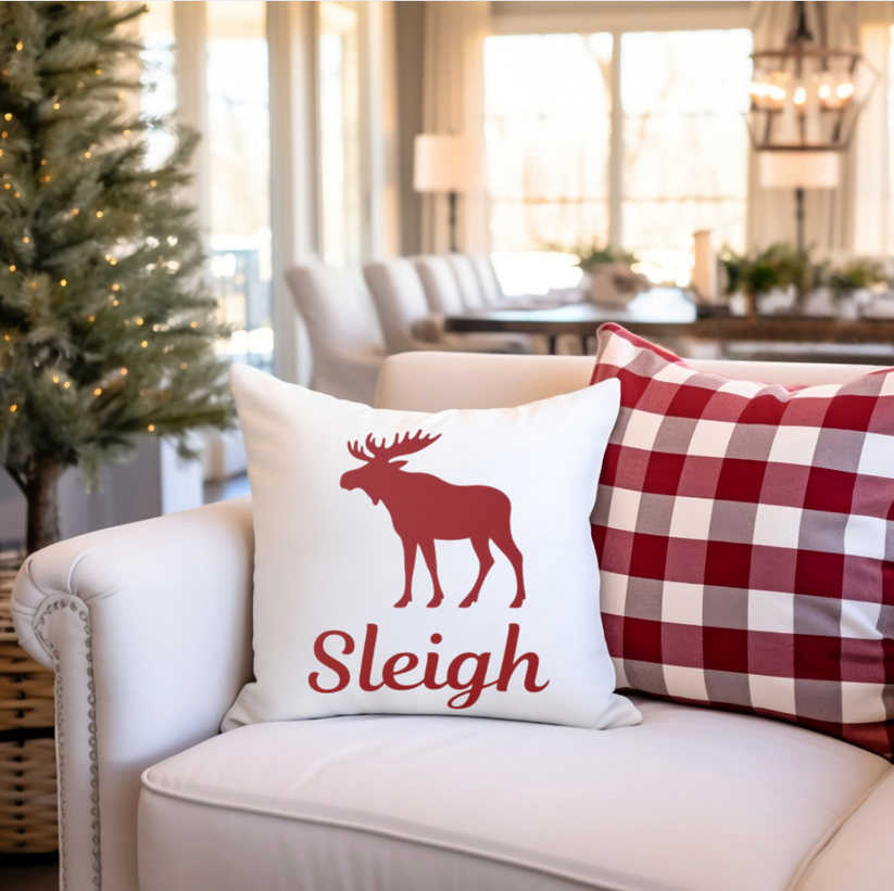 Decorative pillow with a moose design and 'Sleigh' text on a couch in a living room setting.