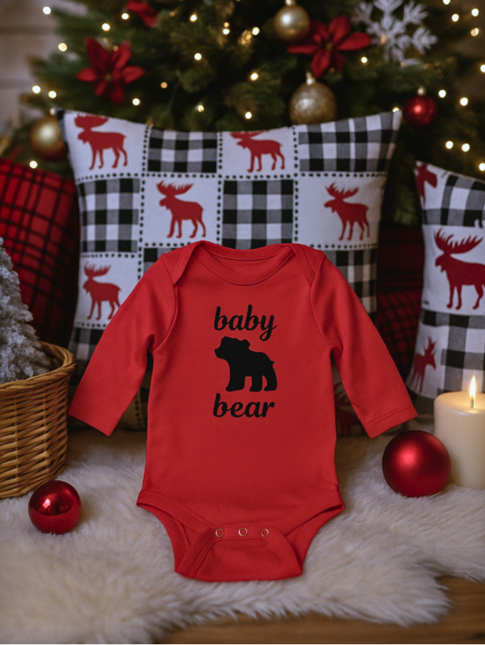Red baby onesie with 'baby bear' print in front of a decorated Christmas tree.