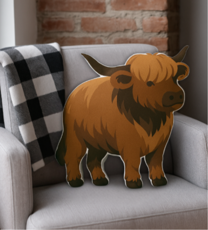 Pillow with a highland cow design on a gray sofa with a checkered blanket.
