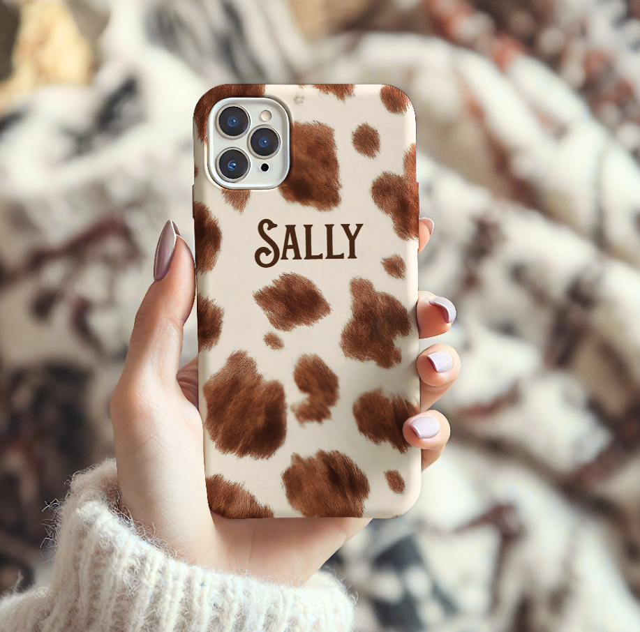 Phone case with cow print pattern and 'SALLY' text held by a person.