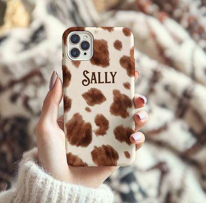 Phone case with cow print pattern and 'SALLY' text held by a person.