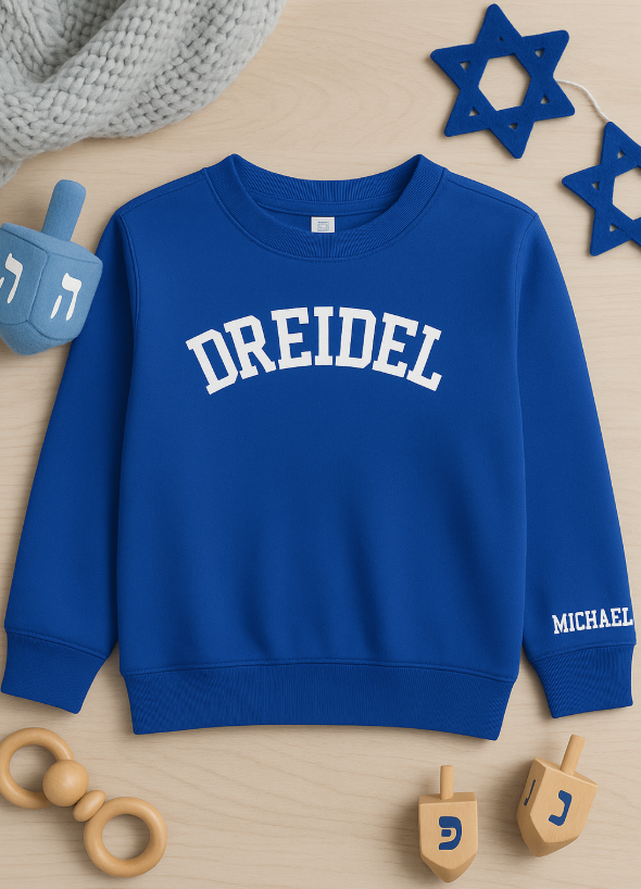Blue sweatshirt with 'DREIDEL' printed on it, surrounded by wooden dreidels and a Star of David, on a wooden surface.