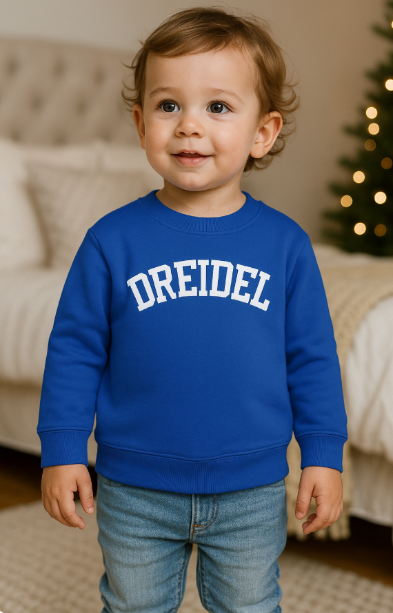 Child wearing a blue sweatshirt with 'DREIDEL' text, standing in a home setting.