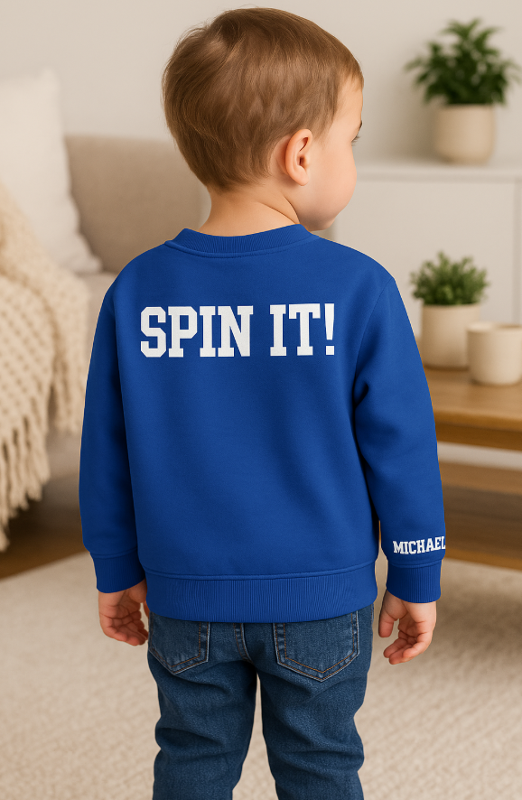 Child wearing a blue sweatshirt with 'SPIN IT!' text in a home setting