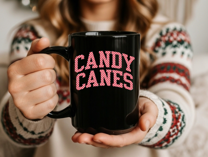 Person holding a black mug with 'CANDY CANES' in pink text, wearing a festive sweater.