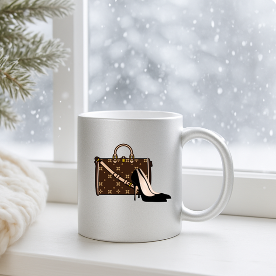 Silver mug with a design of a handbag and high heels on a windowsill with a snowy background.