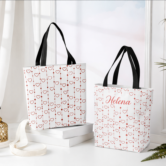 Two tote bags with heart patterns and a name on a white surface.