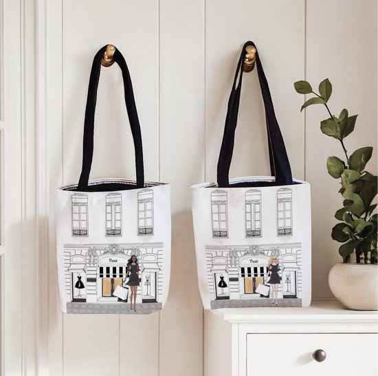Two tote bags with black handles hanging on a white wall.