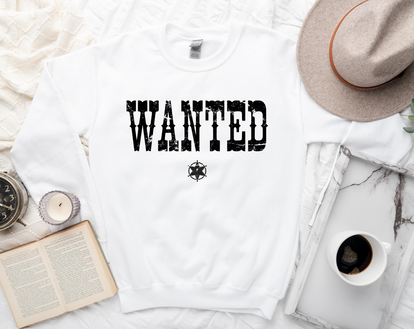 White t-shirt with 'WANTED' text on a white surface with a hat, book, and coffee cup.