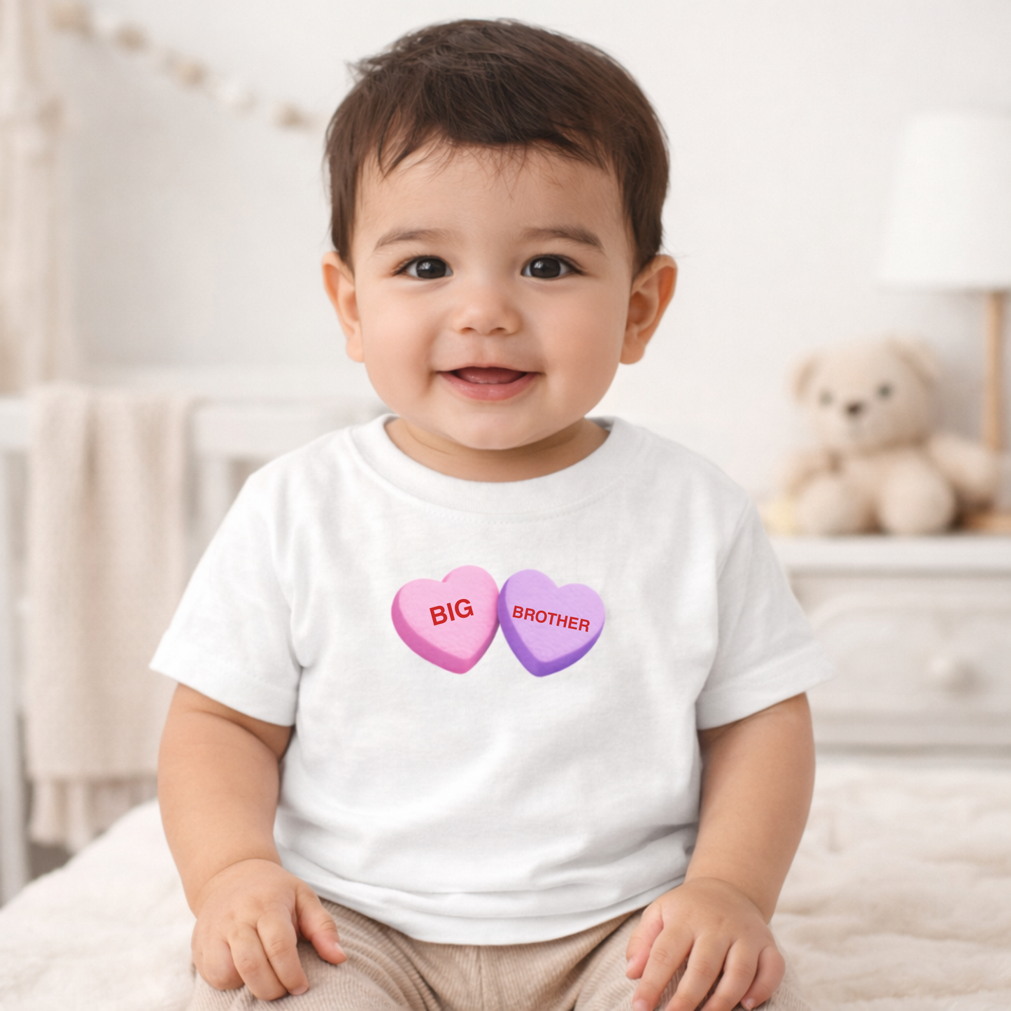 Child wearing a white t-shirt with 'BIG BROTHER' text on a heart design, sitting in a crib.