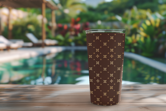 Brown tumbler with a pattern on a wooden table with a pool and greenery in the background